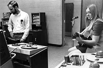 2 people in the recording studio, one is playing the guitar