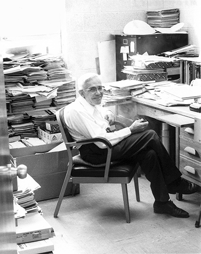 Dr. Clyde Tombaugh sitting at desk, surrounded by piles of work